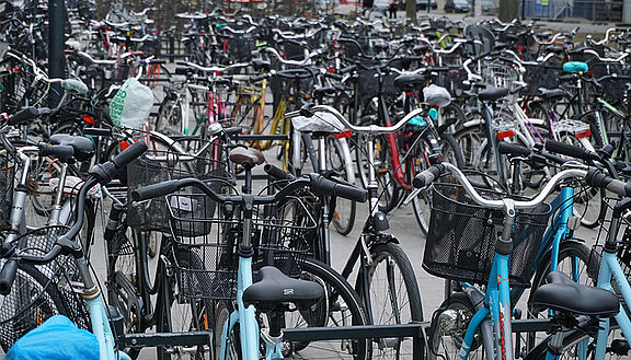 Das Bild zeigt viele geparkte Fahrräder. Die Fahrräder stehen dicht an dicht auf einem Platz nebeneinander.