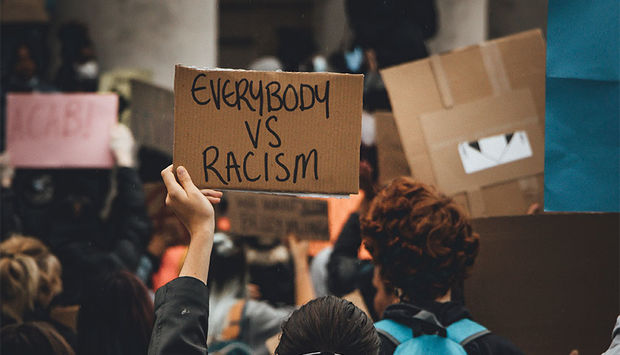 Ein Bild einer Demonstration mit Plakaten. Der Schriftzug "everybody vs. racism" ist zu lesen.