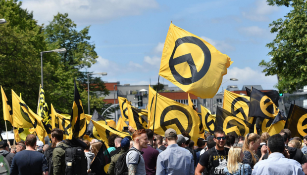 Ein Demonstrationszug von der extrem rechten Identitären Bewegung mit Flaggen mit dem Logo der IB in gelb mit einem Lambda darauf.