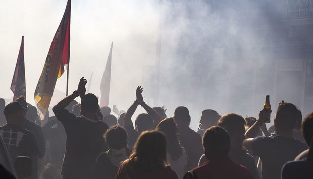 Ein Foto von einem Demonastrationszug mit vielen Menschen mit Fahnen in der Hand. Rauch umgiebt die Menschen. 