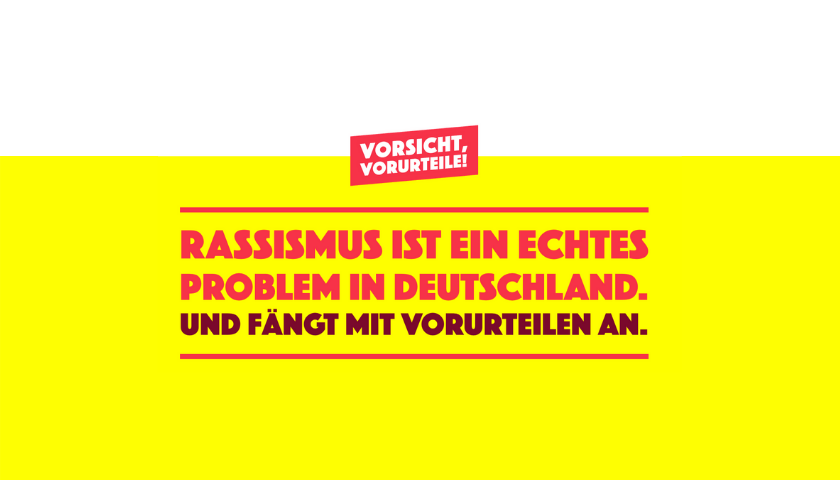 Ein Bild der Plakatkampagne Vorsicht Vorurteil! Darauf steht vor einem gelben Hintergrund mit roter Schrift: Rassismus ist ein echtes Problem in Deutschland und fängt mit vorurteilen an.