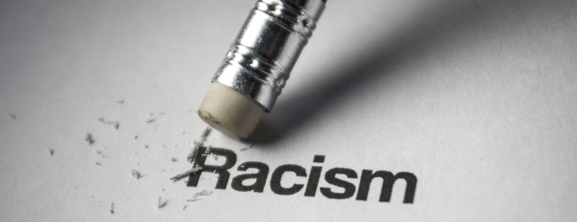Das Bild zeigt ein Blatt Papier, auf dem das Wort Racism steht. Das Wort wird von einem Radiergummi ausradiert.