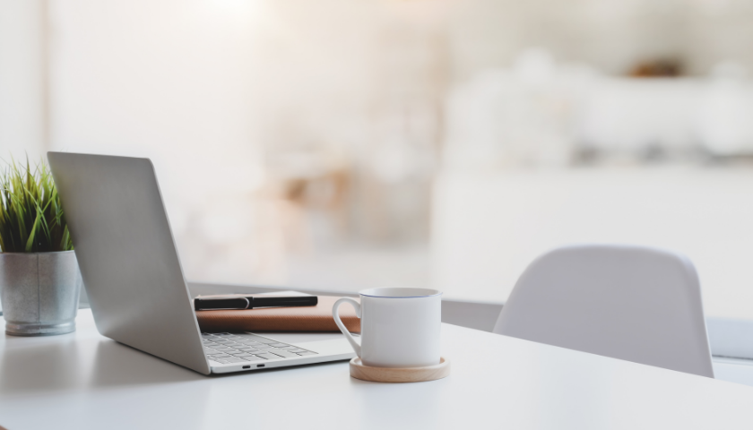 Ein Laptop und eine Kaffeetasse stehen auf einem aufgeräumten Schreibtisch.