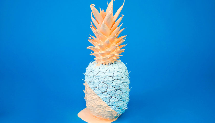 eine mit weißer und rosefarbener Farbe angestrichene Ananas vor blauem Hintergund